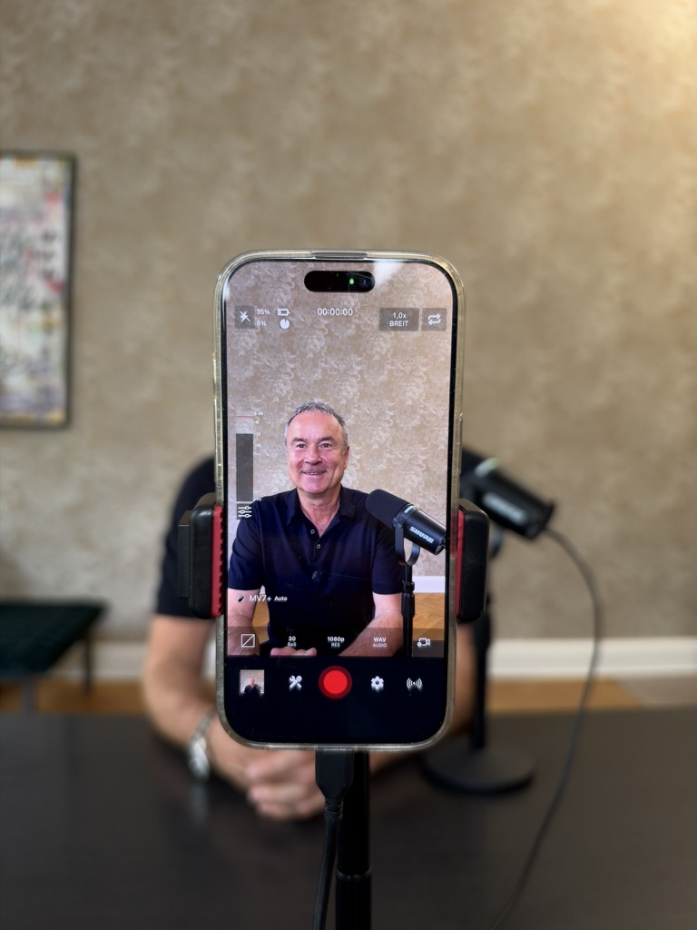 Rechtsanwalt Jörg Franzke bei der Aufnahme einer Briefings-Folge, im Display eines Smartphones neben einem Podcast-Mikrofon